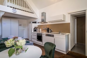 Une cuisine moderne avec des meubles blancs, un coin repas doté d’une table ronde et une chaise verte.