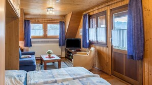 Een houten cabin met een bank, fauteuil, televisie en ramen met gordijnen.