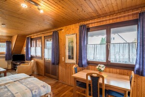 Una stanza con pannelli in legno, un letto, un tavolo con sedie, una televisione e finestre con tende.