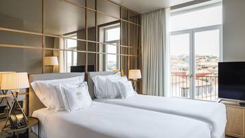 Ein Hotelzimmer mit einem großen Bett, zwei Nachttischen, einem Fernseher und einem Fenster mit Blick auf die Stadt.