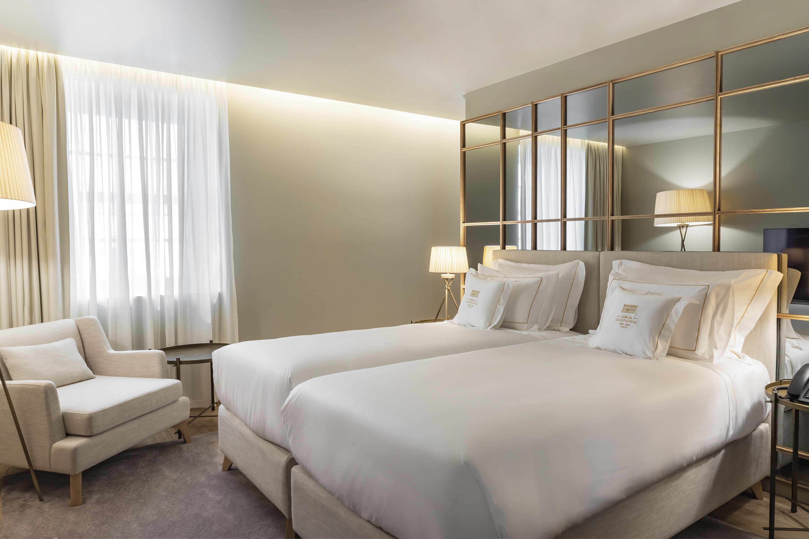 Une chambre d’hôtel avec deux lits, un canapé, un grand miroir et une lampe.