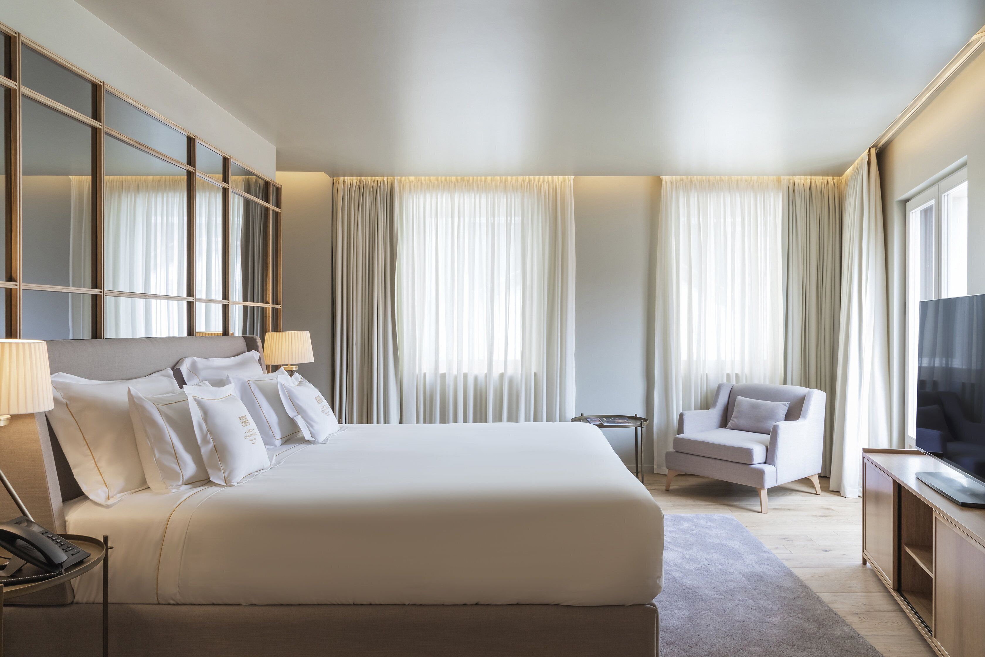 A hotel room with a large bed, a chair, a TV, and curtains.