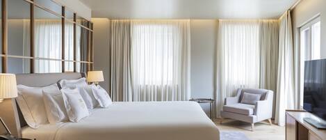 A hotel room with a large bed, a chair, a TV, and curtains.