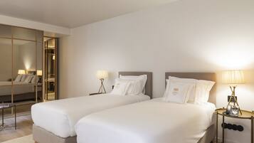 Habitación de hotel con dos camas, un espejo grande, lámparas de noche y una mesita con lámpara.