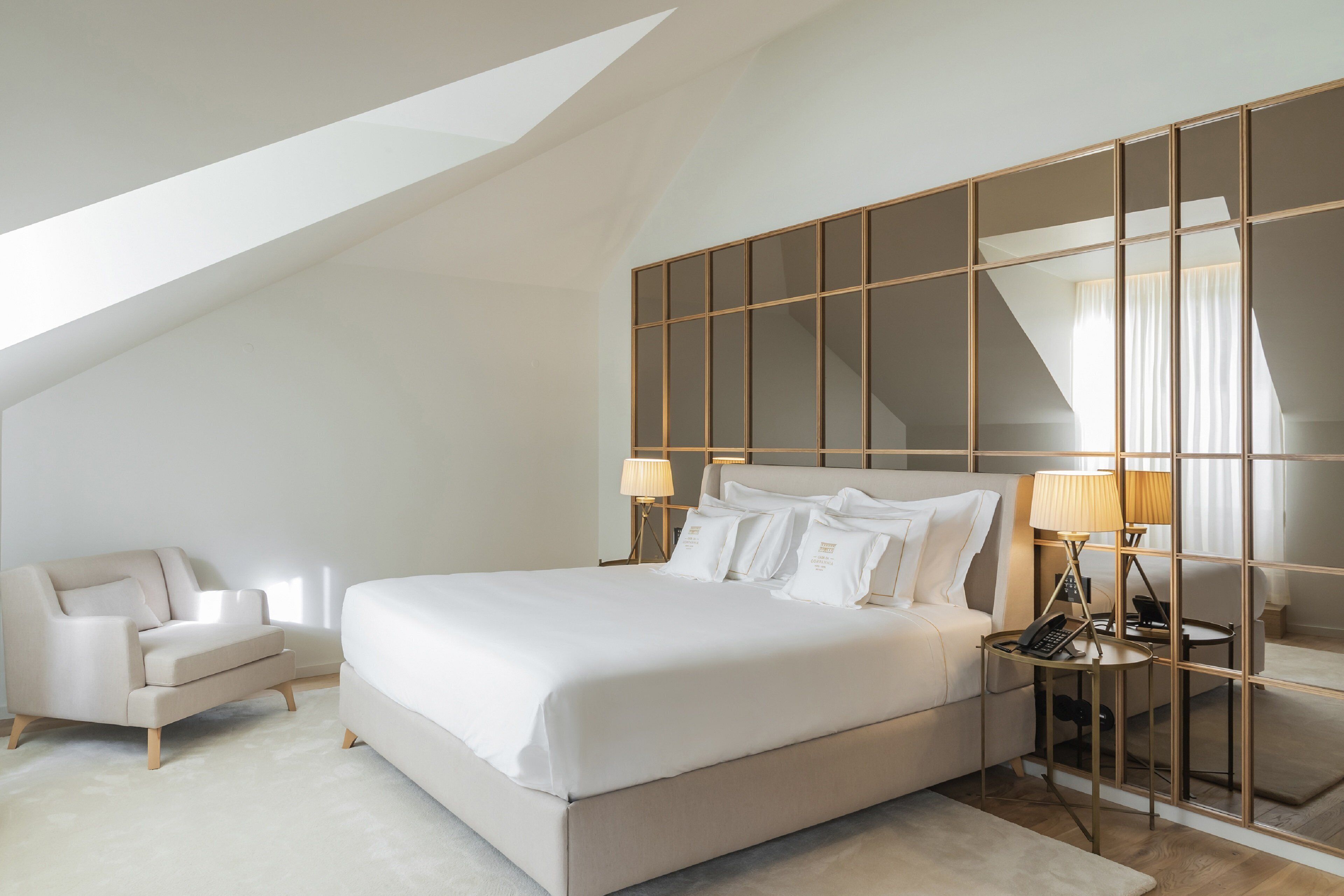 A modern bedroom with a large bed, a sofa, a nightstand with a lamp, and a mirror.