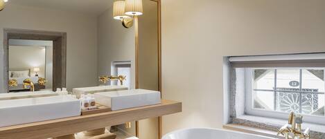 A modern bathroom with a large mirror, two sinks, a bathtub, and a window with decorative ironwork.