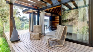Terraza de madera con sillas de mimbre y chimenea, con vistas a un paisaje pintoresco.