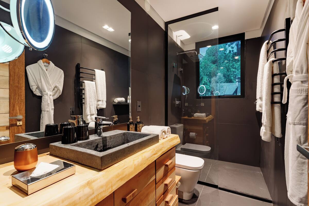 Une salle de bain moderne avec un grand miroir, un meuble-lavabo en bois, un lavabo encastré, des toilettes et un espace douche.