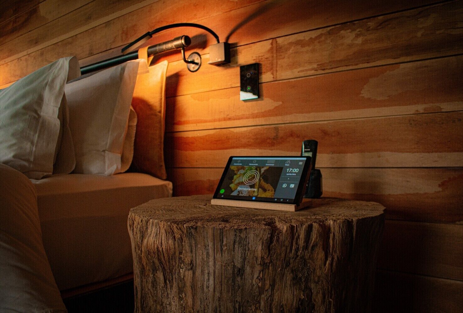 A wooden wall with a mounted device displaying a restaurant menu, a wooden stool, and a sofa with pillows.