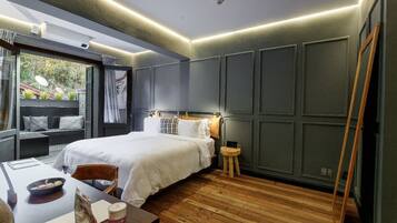 Ein modernes Schlafzimmer mit einem großen Bett, Holzboden, einem kleinen Tisch mit einer Schüssel und einer Tasche sowie Blick auf Grünflächen.