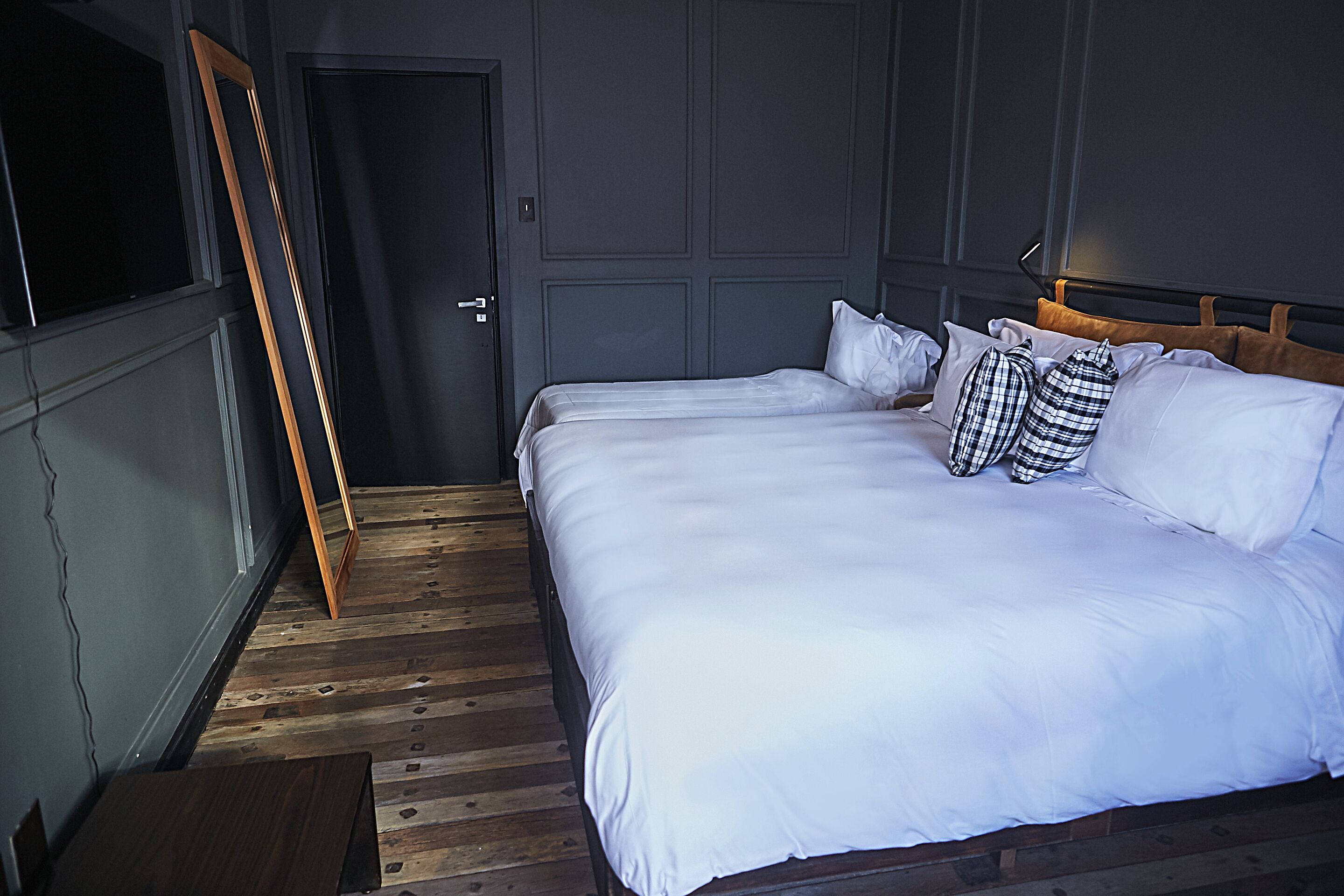Quarto com uma cama grande, piso de madeira, porta e televisão fixada na parede.