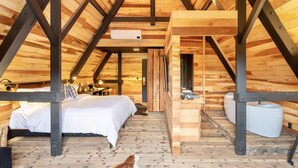 Un dormitorio acogedor en el ático, con techo de madera, cama, escritorio y baño pequeño.