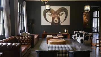 A living room with a large ram head painting, a leather sofa, a coffee table, and a cow-themed armchair.
