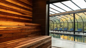 Un espacio con bancos de madera, piscina con cerramiento de vidrio y sillas de lounge azules.