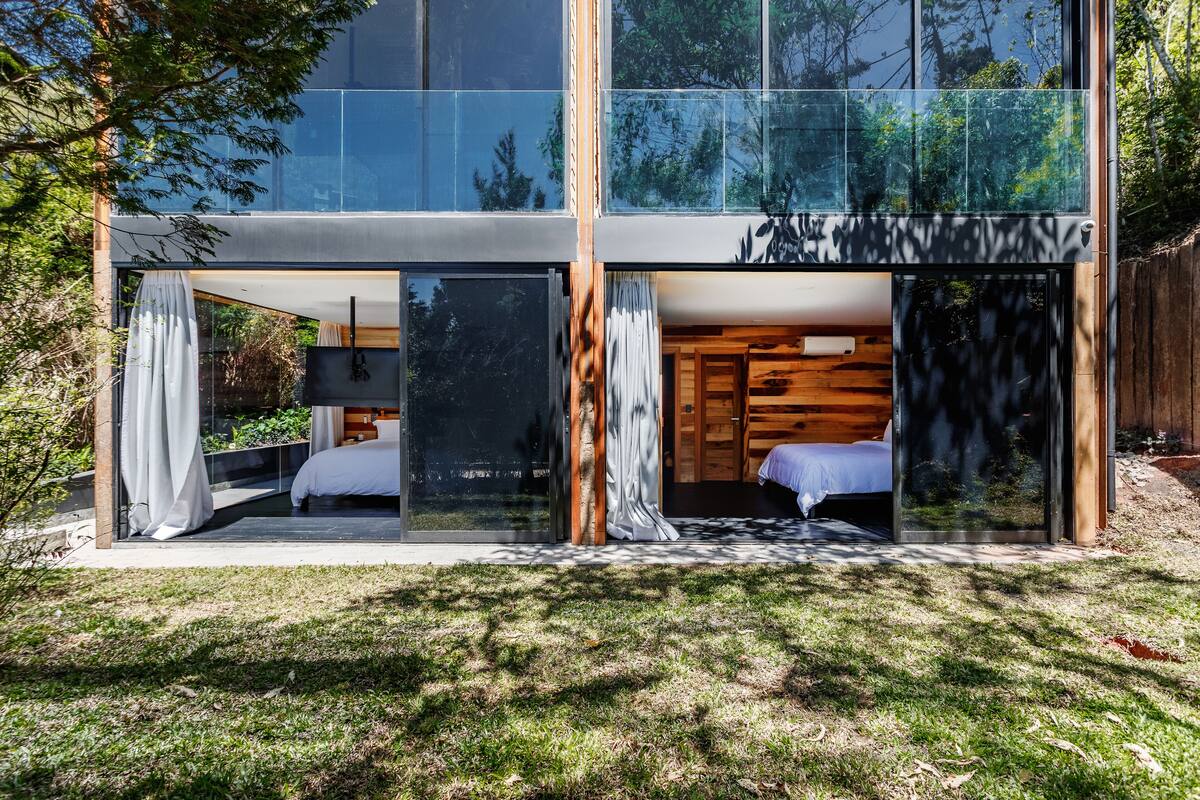 Une maison moderne avec de grandes fenêtres en verre, un intérieur en bois et une cour verdoyante.
