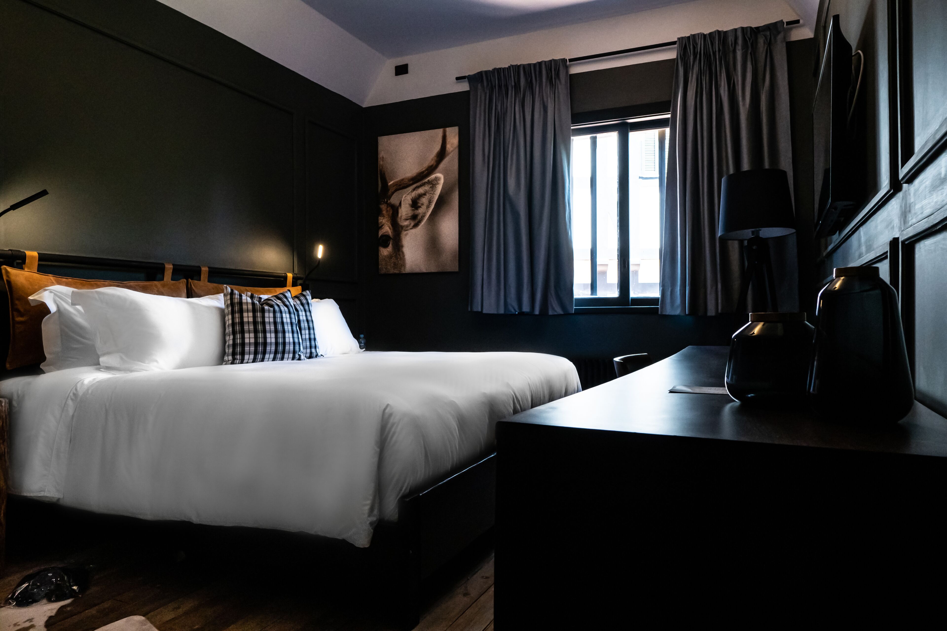 A hotel room with a large bed, a desk, a lamp, and a window with curtains.