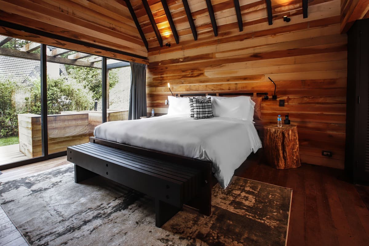 Une chambre à coucher moderne avec un plafond en bois, un grand lit, un banc et un petit tabouret en bois.
