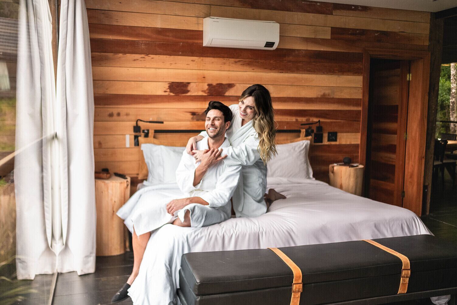 A wooden cabin-style bedroom with a bed, bedside tables, and an air conditioning unit.