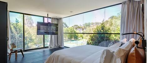 Quarto moderno com cama grande, televisão e vista para o exterior.