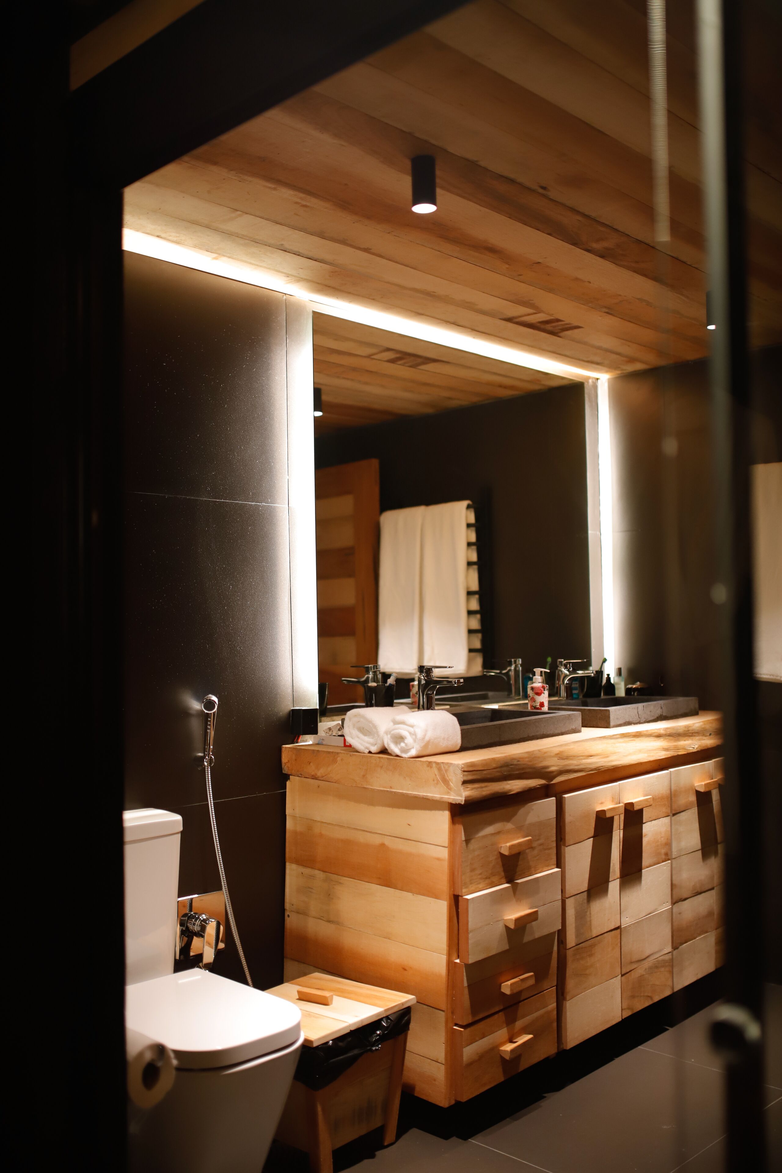A modern bathroom with a wooden vanity, a toilet, and a large mirror.