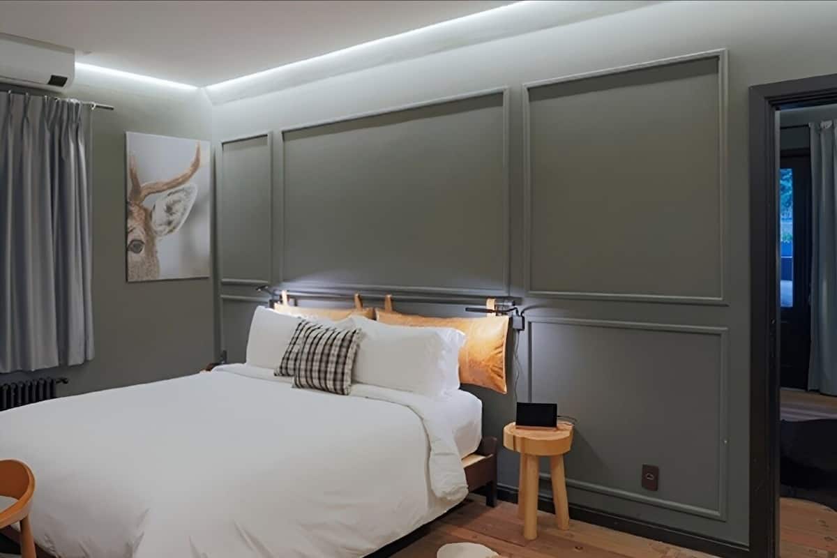 Une chambre à coucher moderne avec un grand lit, une table de chevet, une étagère fixée au mur et une fenêtre avec des rideaux.