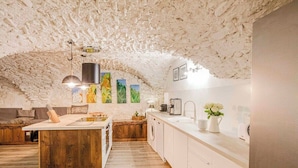 Une cuisine rustique avec un îlot central en bois, des armoires blanches et un plafond en pierre.