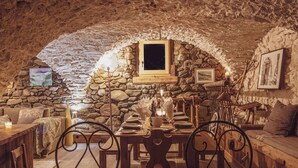 Une pièce rustique aux murs de pierre, avec une table à manger en bois, des chaises et un coin salon confortable.
