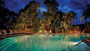 Piscina com espreguiçadeiras e vegetação tropical.