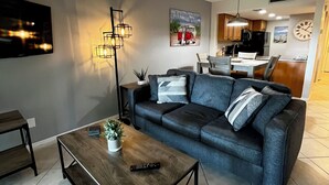 Uma sala de estar moderna com uma mesa de centro em madeira escura, um sofá cinza e um ventilador de teto.