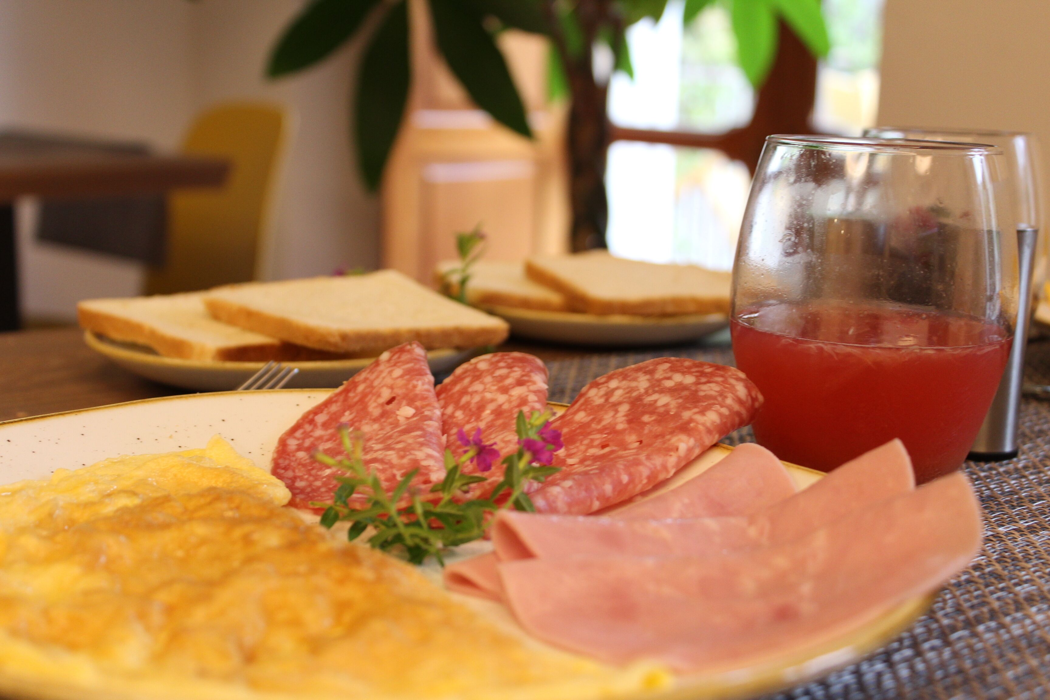 Ein Frühstücksteller mit Eiern, Schinken, Salami und einem Glas roter Saft.