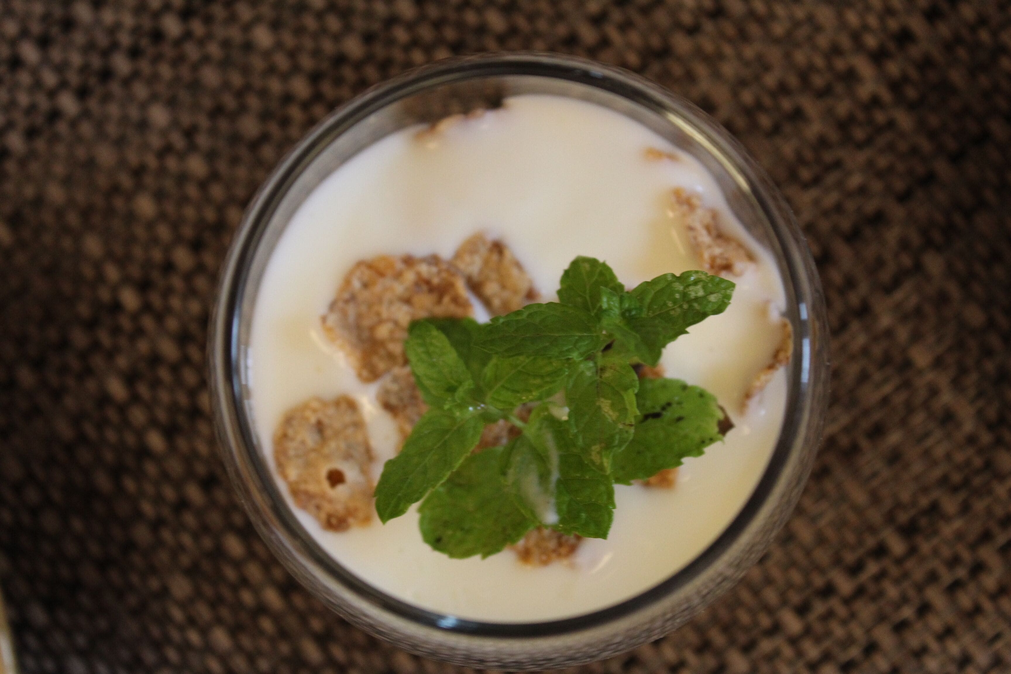 Un verre de lait avec des céréales et une feuille de menthe, le tout posé sur une surface texturée.