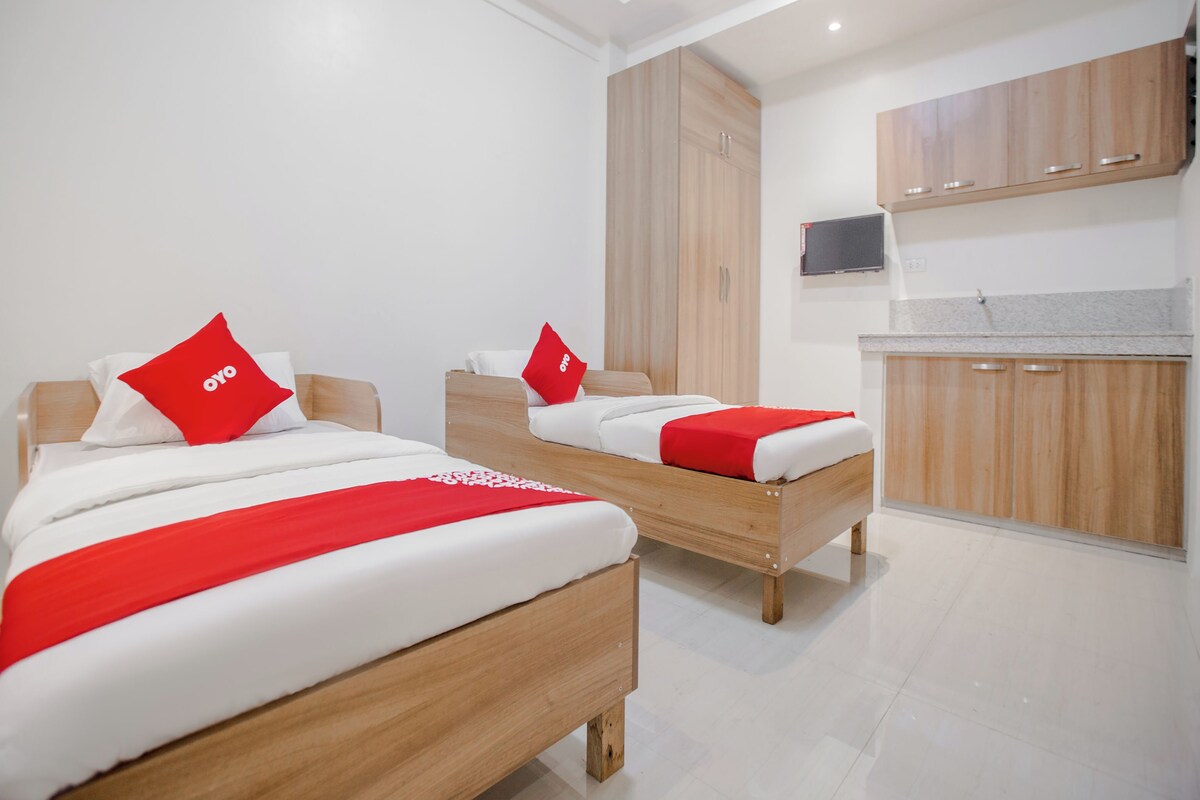 A hotel room with two wooden beds, each with a red and white bedspread, and a television mounted on the wall.