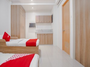 Une chambre d’hôtel avec deux lits, une petite kitchenette et un téléviseur fixé au mur.