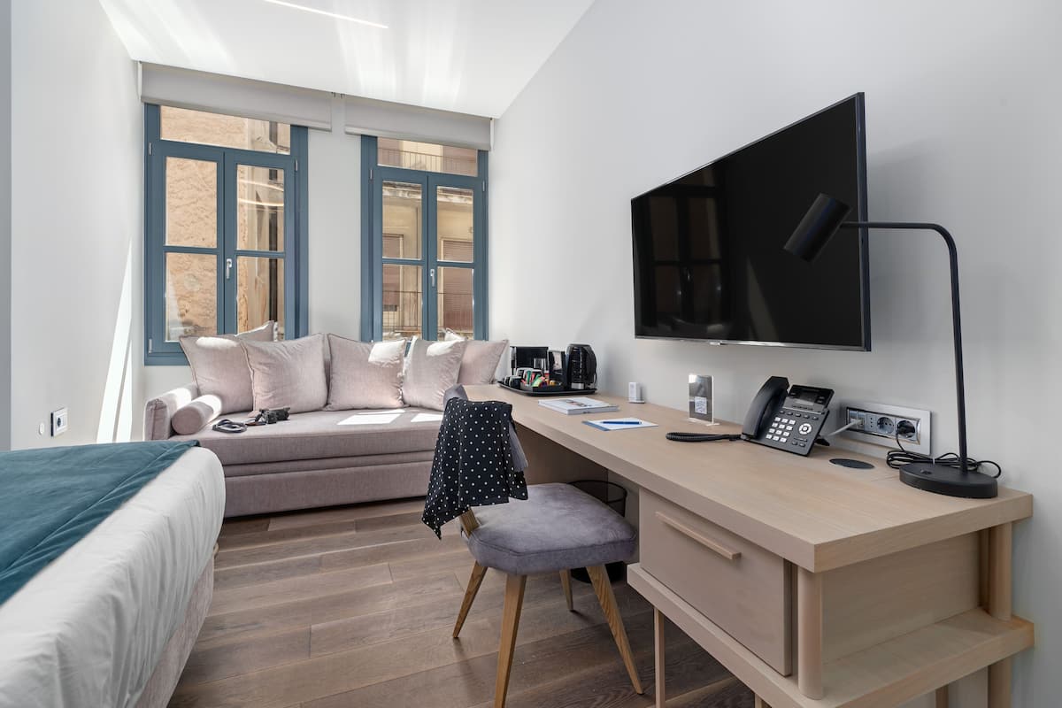 A modern bedroom with a bed, a desk with a computer, a chair, and a TV.