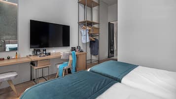 A modern hotel room with a bed, a desk with a flat-screen TV, a chair, a hanging clothes rack, and a wardrobe.