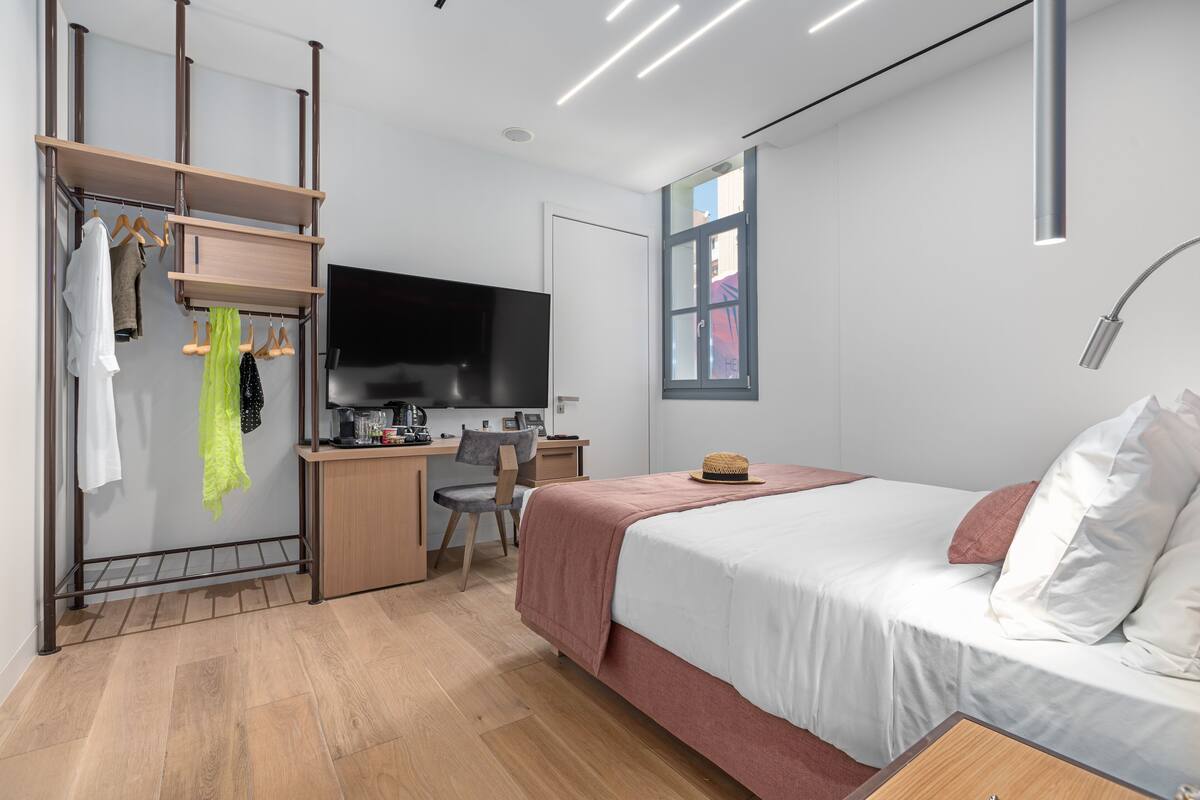 A modern bedroom with a bed, desk, chair, and a TV.