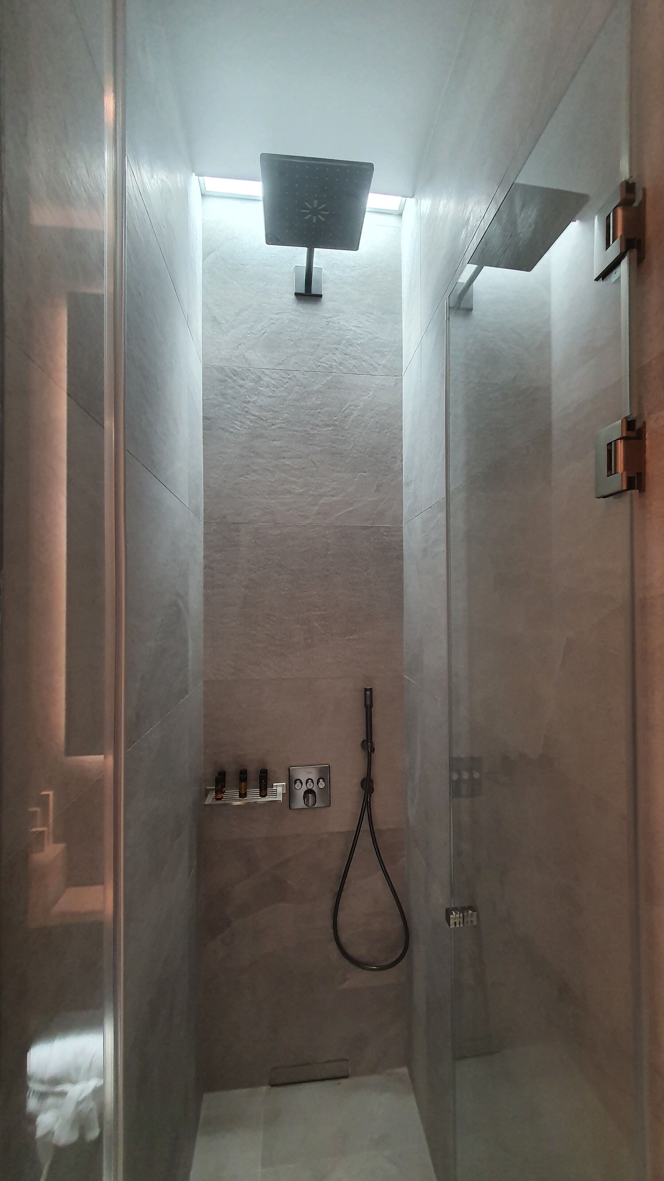 Una doccia moderna con porta in vetro, soffione a mano e pannello comandi con diverse funzioni.