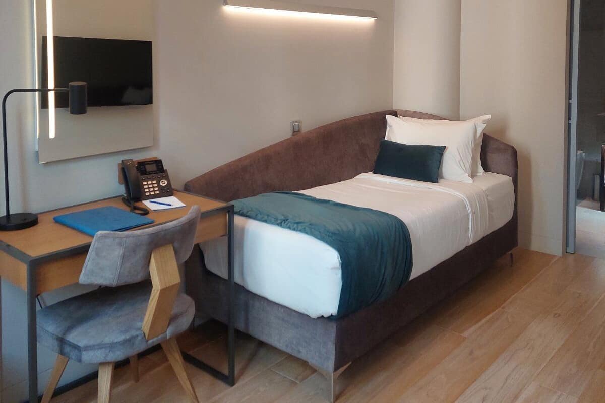 A modern hotel room with a bed, desk, chair, and a large mirror.