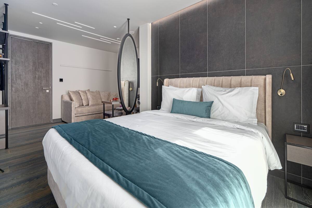 A modern hotel room with a large bed, a bedside table, a wall-mounted mirror, and a built-in wardrobe.