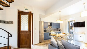 A modern kitchen with stainless steel appliances, a dining area with a wooden table and chairs, and a living area with a sofa and cushions. - Philoxenia Villas (Mylopotamos)