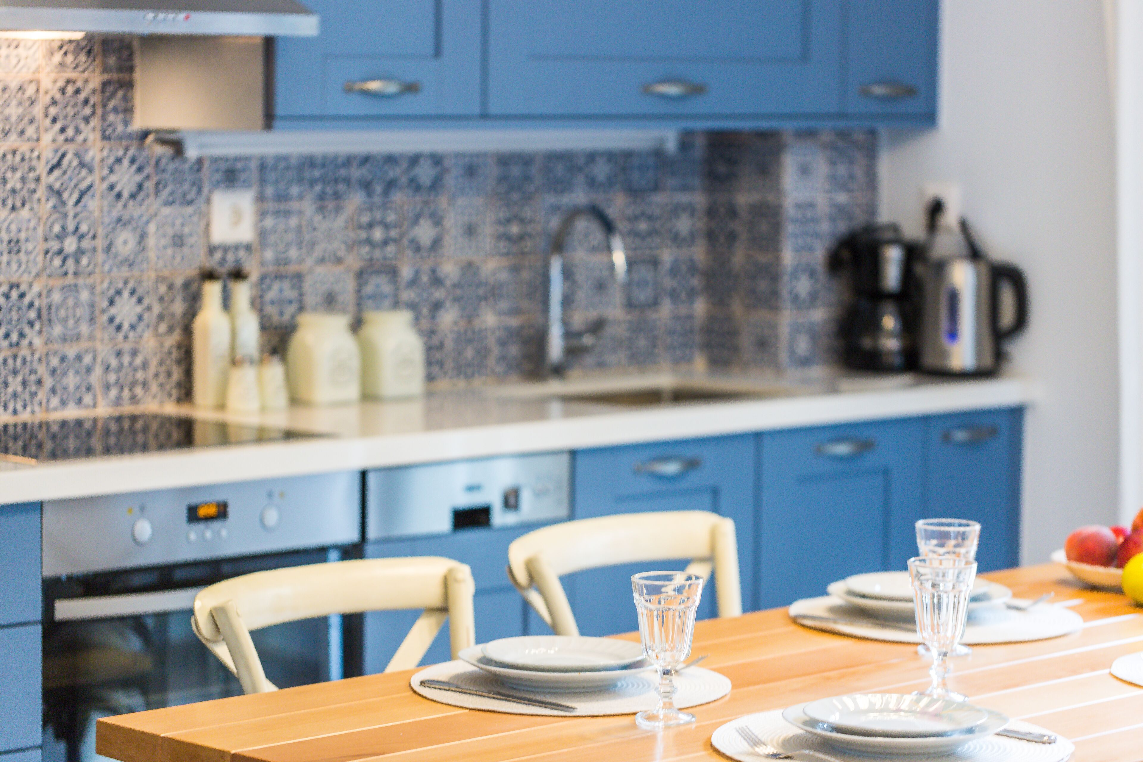 Een keuken met blauwe kastjes, een betegelde spatwand en een houten eettafel gedekt met borden, glazen en bestek.