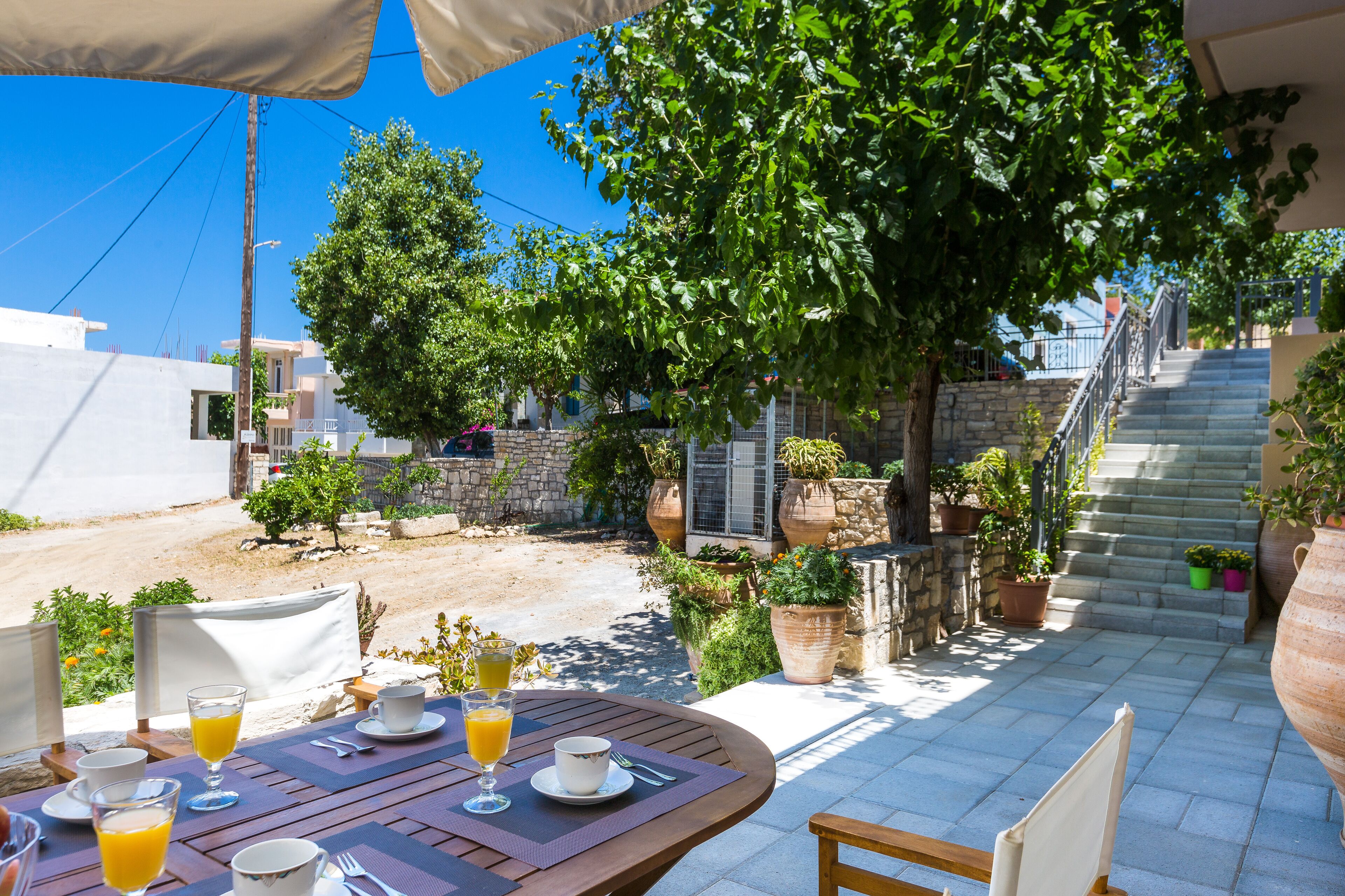 Eine Terrasse im Freien mit Frühstückstisch, umgeben von Blumentöpfen und einer Treppe zu einem Gebäude.