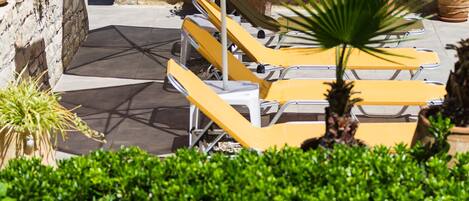 A patio area with yellow lounge chairs and a yellow umbrella, surrounded by potted plants and a stone wall.