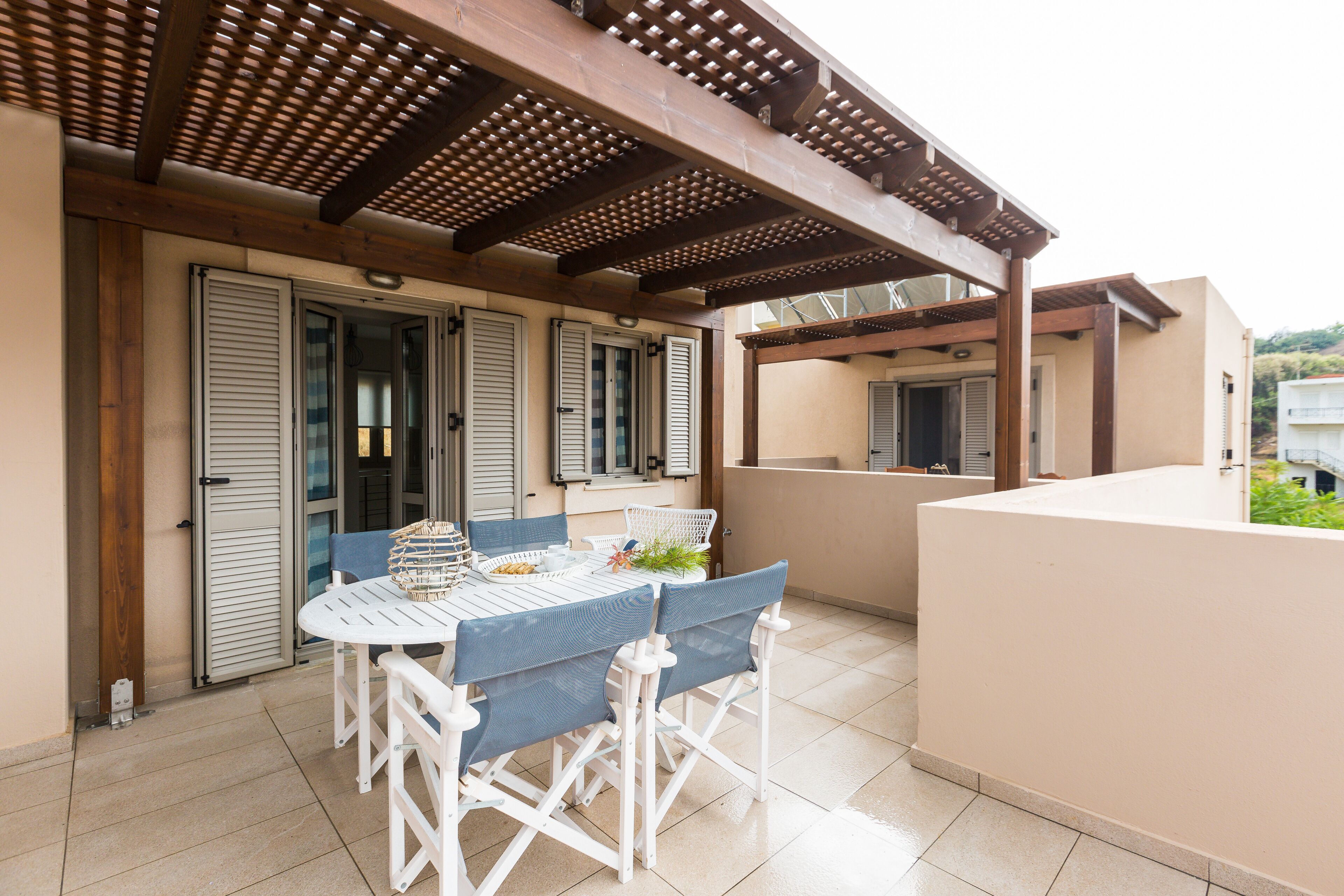 A covered outdoor patio with a table and chairs, a pergola overhead, and a view of a residential area.