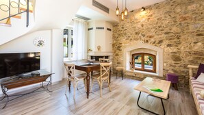 A spacious living area with a stone wall, a fireplace, a dining table with chairs, and a television on a glass stand. - Philoxenia Villas (Mylopotamos)