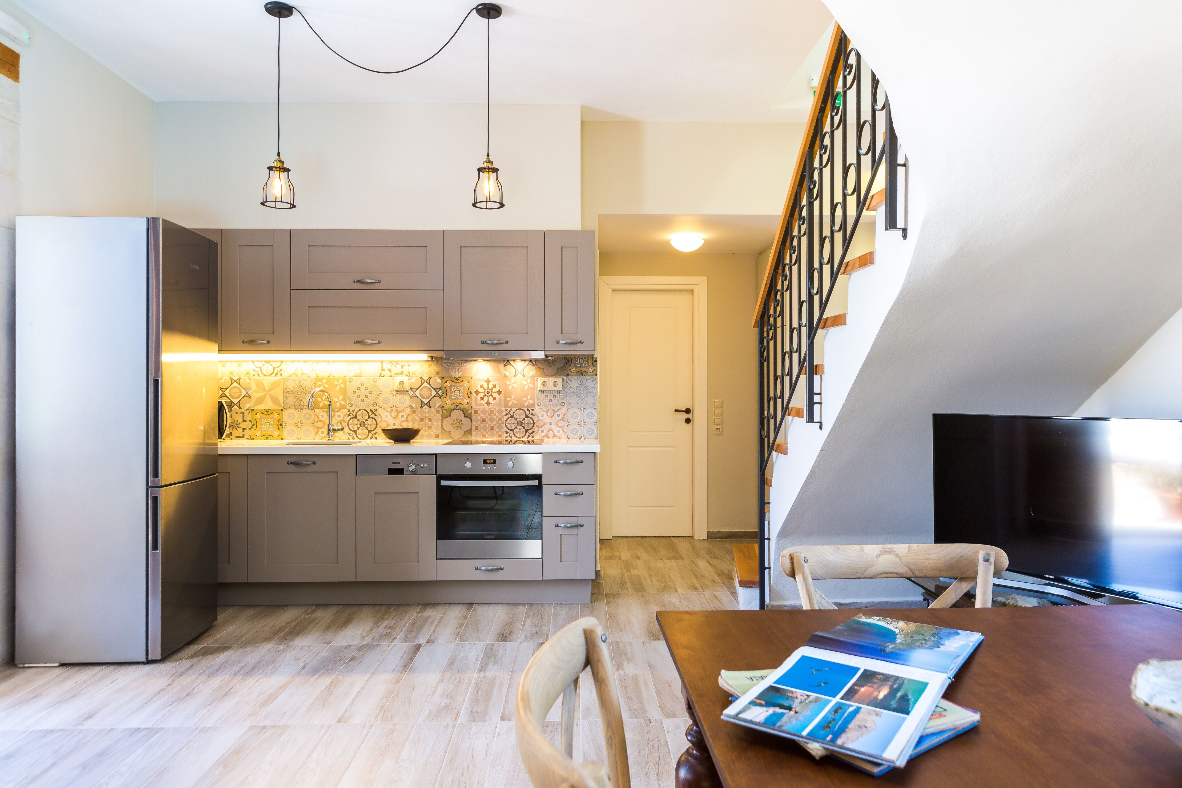 A modern kitchen with grey cabinets, a stainless steel refrigerator, and a dining area with a wooden table and chairs.