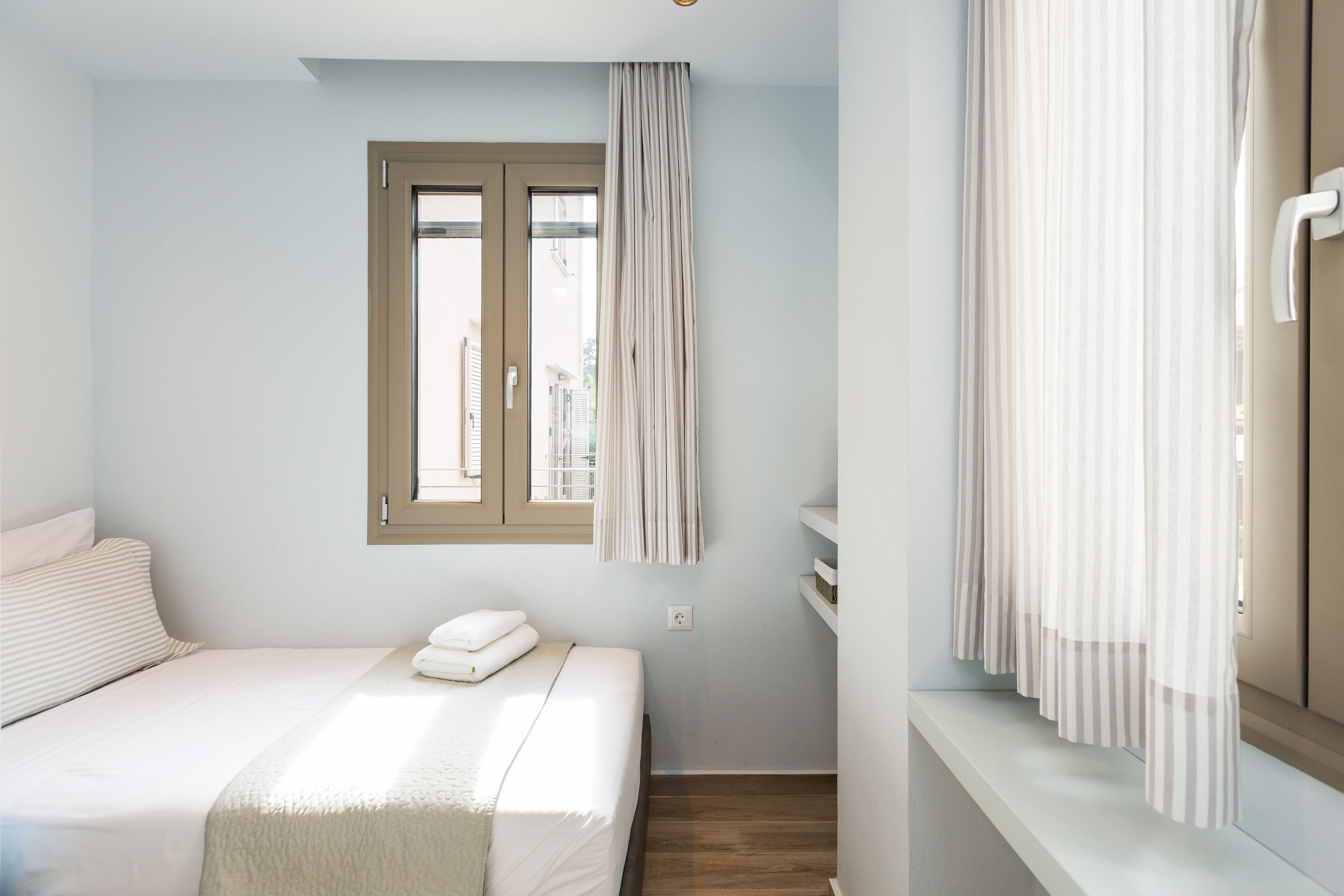 Un dormitori amb un llit, una finestra amb cortines i una paret blanca.