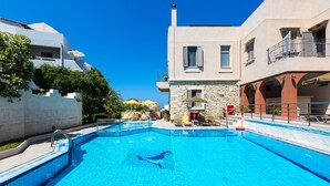 A swimming pool with clear blue water, surrounded by buildings with balconies and outdoor seating. - Philoxenia Villas (Mylopotamos)