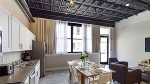 Een moderne keuken met roestvrijstalen apparatuur, een eethoek met een tafel gedekt voor vier personen, en grote ramen met gordijnen.