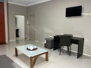 A modern room with a glass-top table, a black desk, a chair, and a television mounted on the wall.